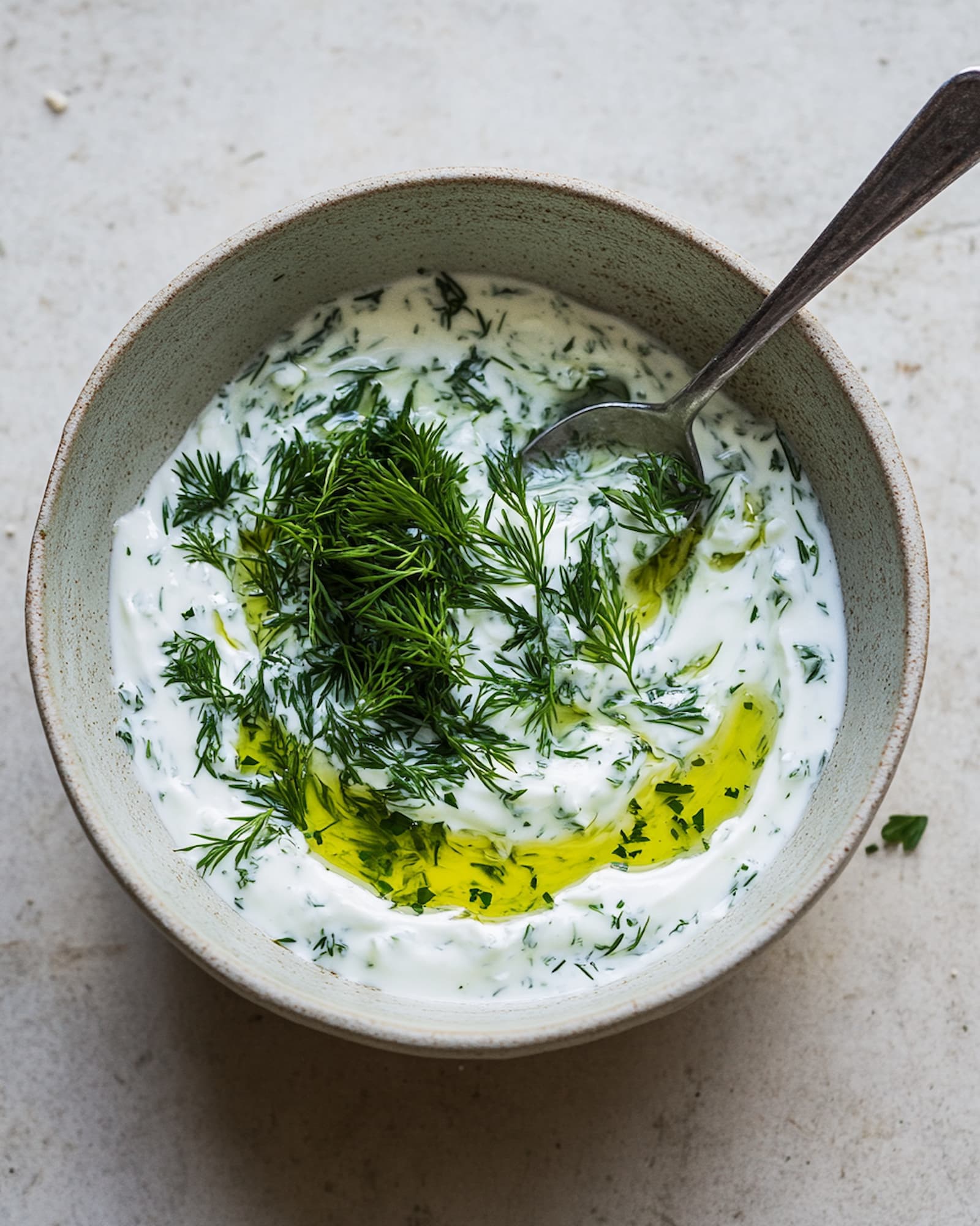Grüner Kräuterjoghurt in einer Keramikschale mit Dill, gehackter Petersilie und Olivenöl, von oben